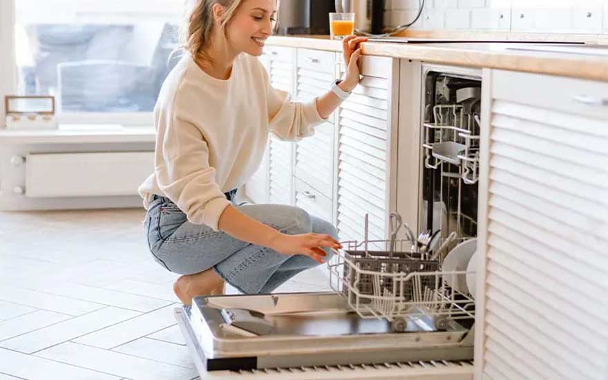 Een keuken met witte kasten en een open vaatwasser. Binnenin staan rekken met borden en bestek. De vloer heeft een licht tegelpatroon.