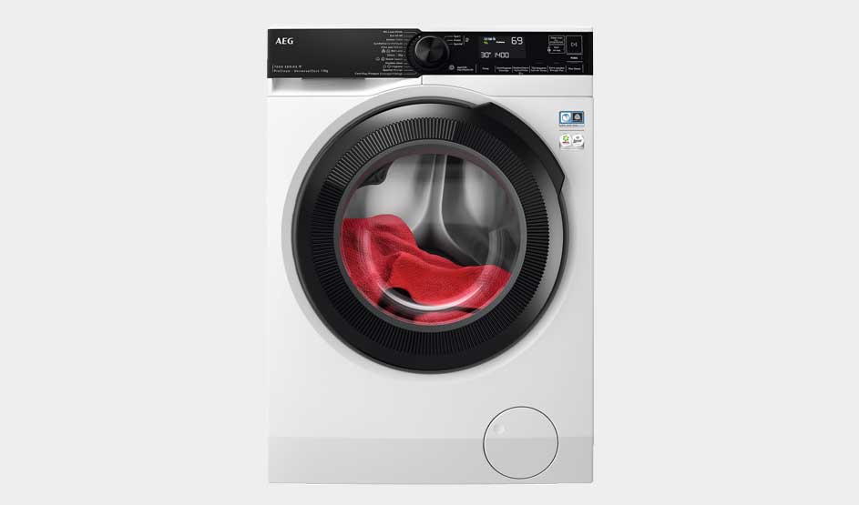Een witte AEG wasmachine draait een rode handdoek. Het digitale scherm toont het programma in een moderne, minimalistische ruimte.