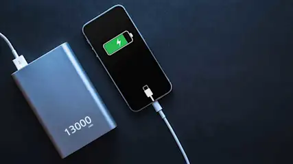 Un téléphone noir se charge depuis une batterie externe grise de 13000 mAh sur un fond sombre.