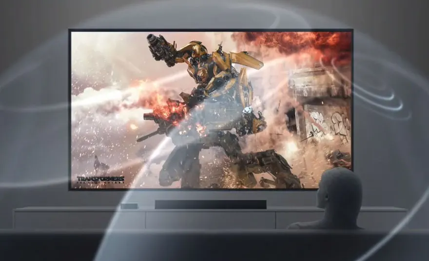 Un écran TV affiche un robot Transformers jaune sur fond de feu. Le téléviseur est placé sur un meuble blanc.