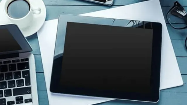 Bureau met laptop, tablet met zwart scherm, koffie, bril en telefoon op blauwe houten achtergrond.