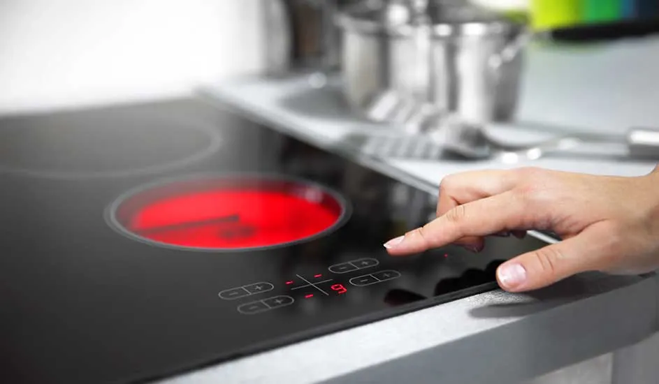 Une main touche une plaque de cuisson noire. Un cercle rouge indique la chaleur. Des ustensiles sont en arrière-plan.