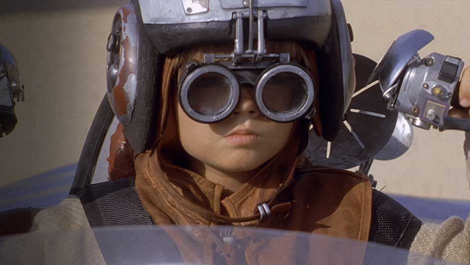 Gros plan d'un casque gris et de lunettes rondes. Les mains sont sur des commandes argentées. L'arrière-plan est beige.