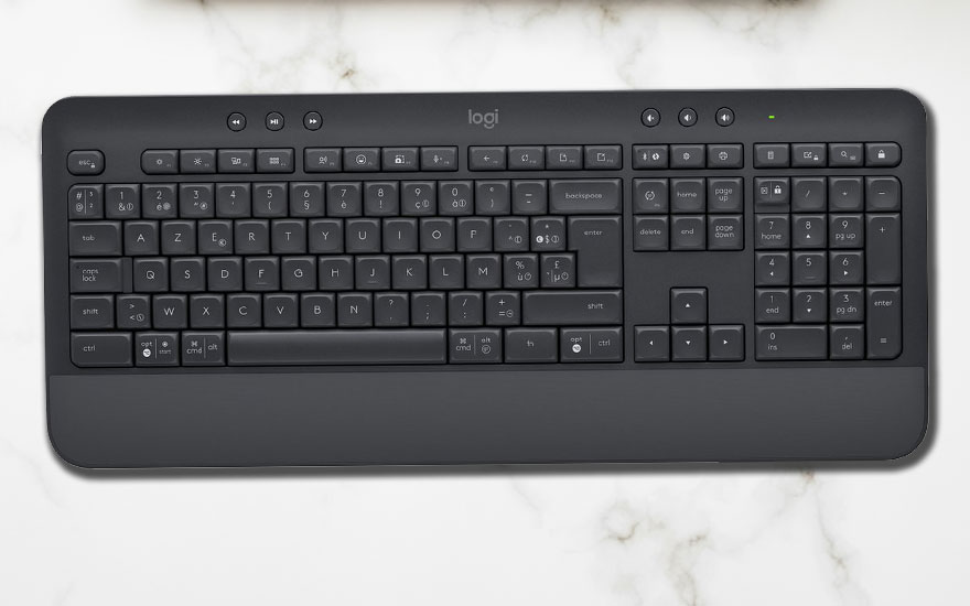 Een donkergrijs Logitech-toetsenbord ligt op een witte marmeren achtergrond. Het toetsenbord heeft een numeriek toetsenblok en mediatoetsen bovenaan.