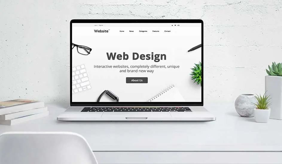 Ordinateur ouvert sur bureau blanc affiche “Web Design”, entouré de livres et de petites plantes vertes devant un mur clair.