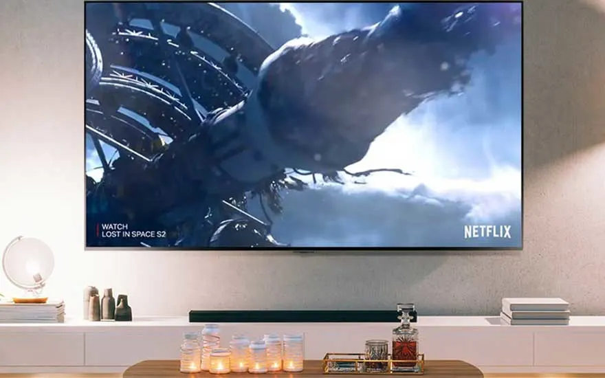 Een tv toont een scène van 'Lost in Space' op Netflix. Voor de tv staat een witte kast met decoraties en een houten tafel.