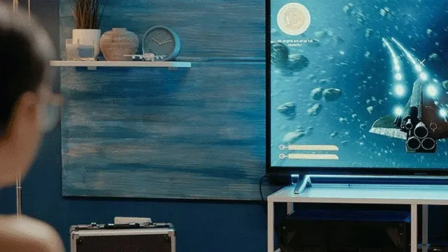 Écran TV affichant un vaisseau spatial dans un jeu, sur un meuble blanc. Décor bleu avec étagère, vase, plante et horloge.