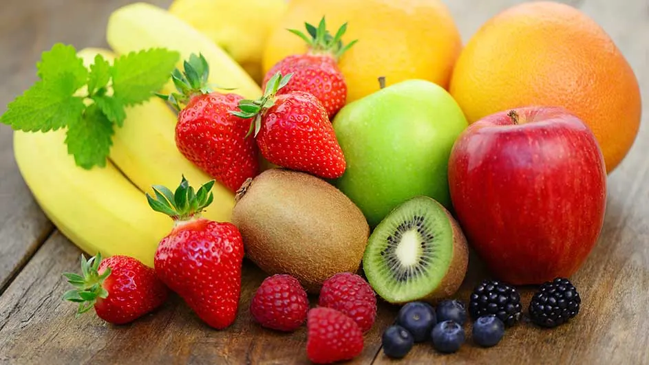 Een assortiment fruit op een houten ondergrond. Bananen, aardbeien, kiwi, appels, sinaasappels, frambozen, blauwe bessen en bramen zijn zichtbaar.