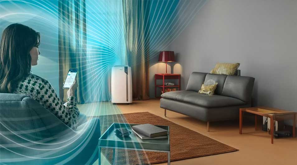 Salon avec canapé gris, table basse, purificateur d'air blanc et rideaux rayés bleus. Lignes bleues illustrant le flux d'air.