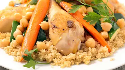 Een bord couscous met kip, wortelen, kikkererwten, courgette en peterselie.