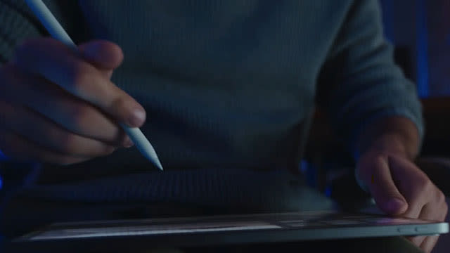 Hand met stylus boven een tablet, in blauw getinte belichting.