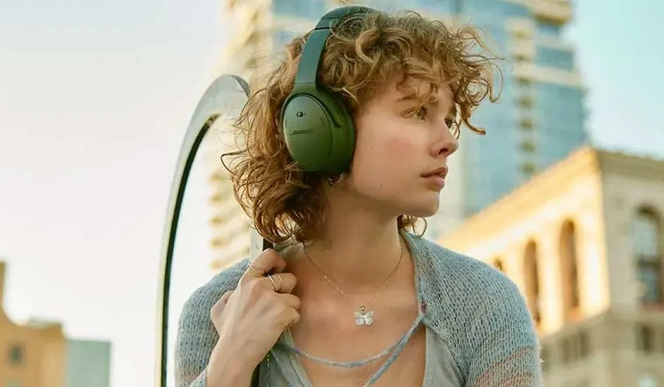 Une femme porte un casque vert. Des bâtiments sont visibles en arrière-plan. Elle a des bijoux.