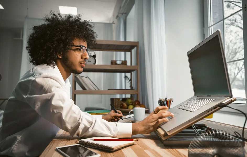Un bureau avec un ordinateur portable ouvert, un bloc-notes, un téléphone et une tasse blanche devant une fenêtre.