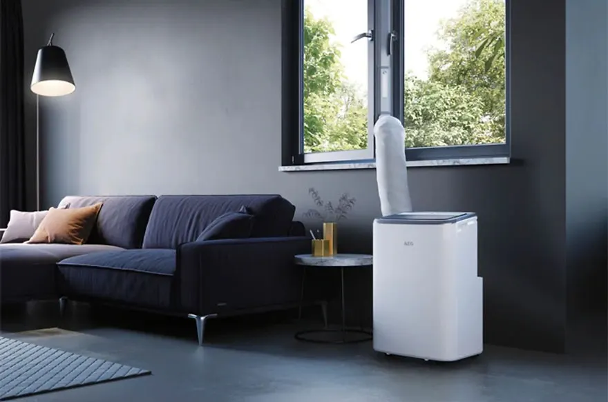 Living room interior with a blue sofa, a white portable air conditioner by a window, and a hanging lamp.