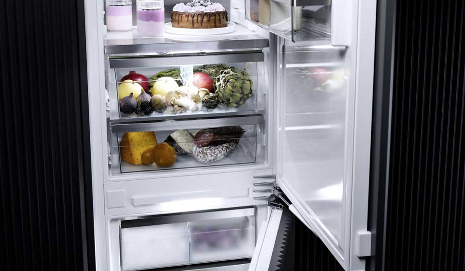 Un réfrigérateur ouvert montre des fruits, des légumes, du fromage et de la charcuterie sur des étagères éclairées.