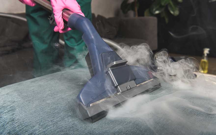 Nettoyage à la vapeur d'un canapé bleu avec un appareil bleu. De la vapeur blanche est visible.