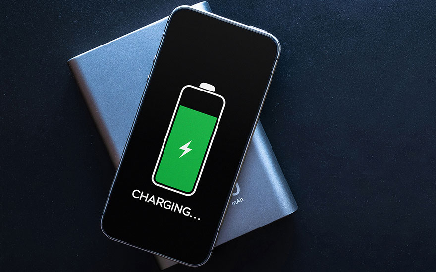 Een zwarte smartphone met een groen batterij-icoon "Charging..." ligt op een zilveren powerbank tegen een donkere achtergrond.