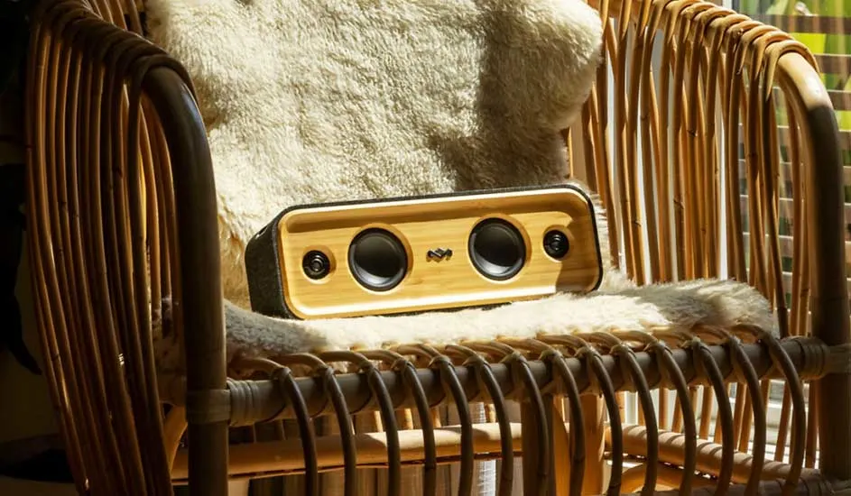 Een houten speaker ligt op een stoel met een zacht kussen. De stoel is gemaakt van bruin riet.