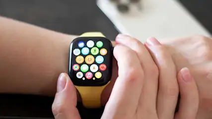 Une montre intelligente à écran noir, bracelet jaune, affichant des icônes d'applications colorées, portée au poignet.