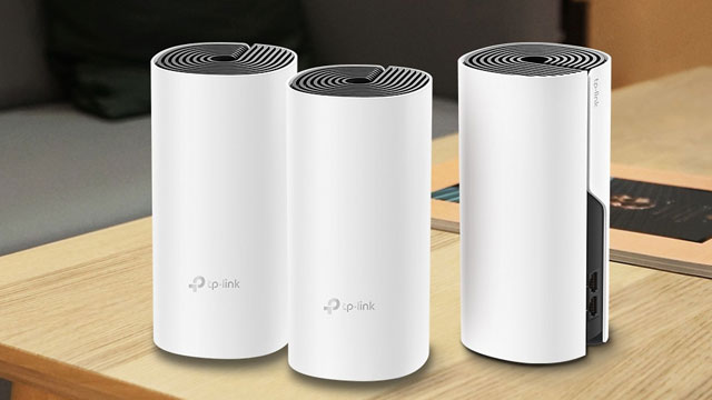 Trois routeurs blancs cylindriques de TP-Link sur une table en bois clair avec un livre en arrière-plan.