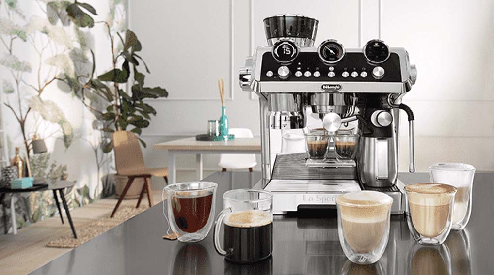 De’Longhi espressomachine op een keukenaanrecht met verschillende kopjes koffie ervoor, van espresso tot cappuccino.