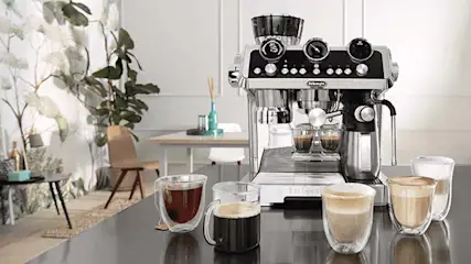 De’Longhi espressomachine op een keukenaanrecht met verschillende kopjes koffie ervoor, van espresso tot cappuccino.