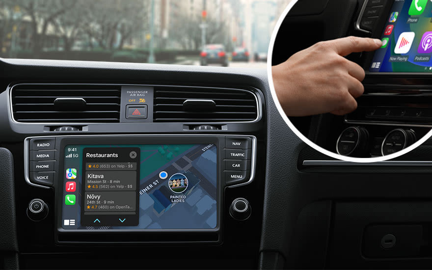 Dashboard van een auto met navigatiescherm waarop restaurants en een kaart te zien zijn. Een hand bedient een ander scherm.