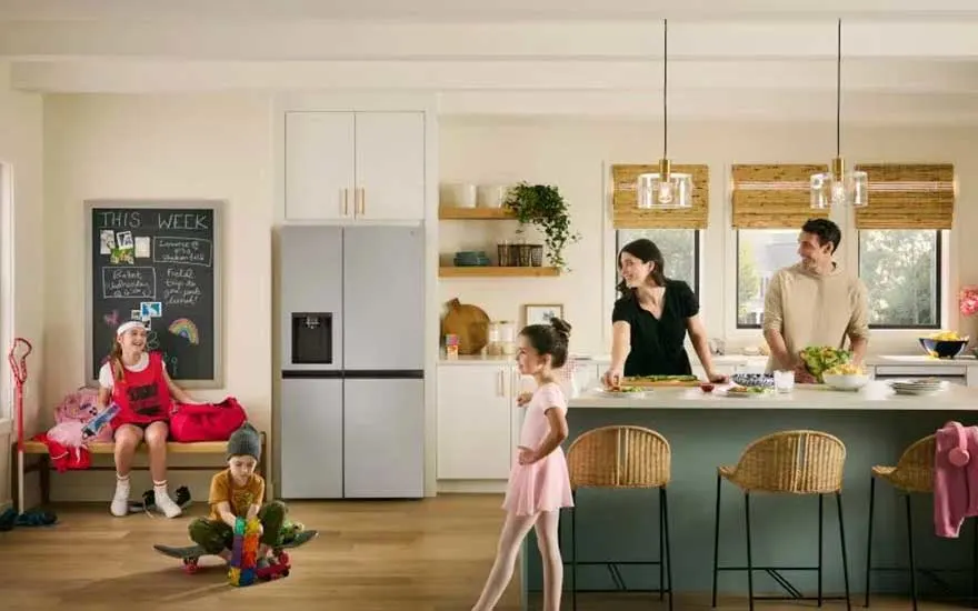 Een gezin is in een lichte keuken: kinderen spelen bij de koelkast en volwassenen bereiden eten aan het eiland met hoge stoelen.