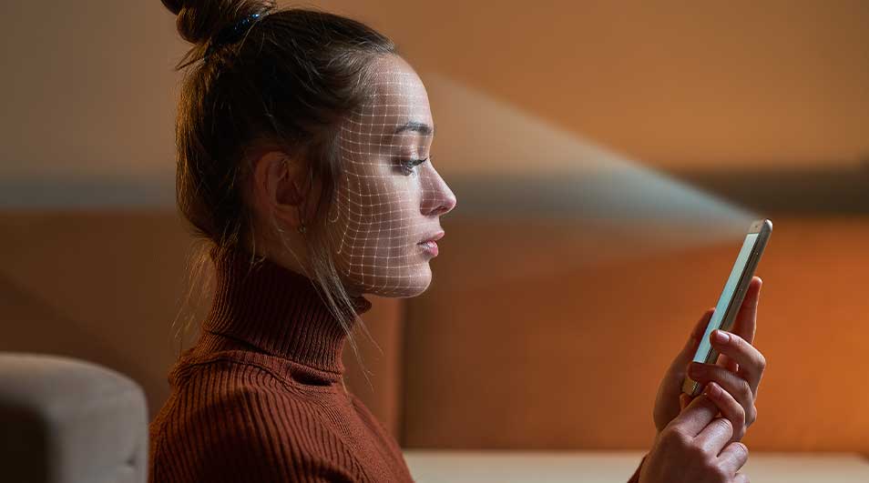 Une personne tient un smartphone. Un motif de grille est projeté sur le visage. Le fond est de couleur marron clair.