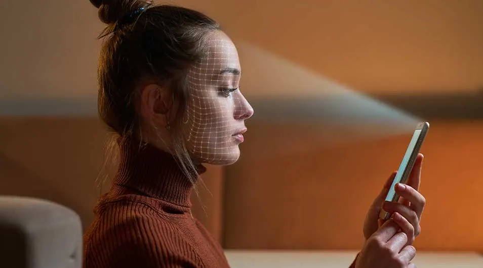 Une personne tient un smartphone. Un motif de grille est projeté sur le visage. Le fond est de couleur marron clair.