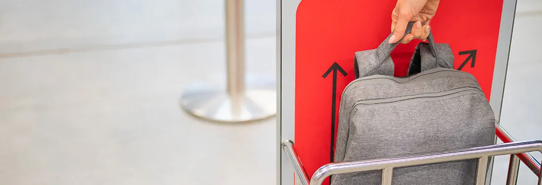 Un sac gris est placé sur un chariot en métal devant un panneau rouge avec des flèches noires.