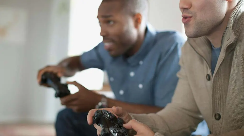 Twee personen houden zwarte gamecontrollers vast. De achtergrond is een vage kamer met witte muren.