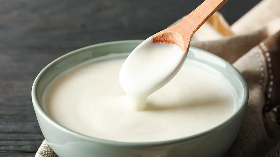 Bol vert rempli de liquide blanc crémeux. Une cuillère en bois est plongée dans le bol, reposant sur un tissu beige.