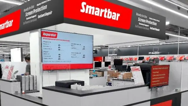 Un comptoir Smartbar dans un magasin. Un écran affiche les prix. Des panneaux rouges et noirs indiquent "Screen Protection".