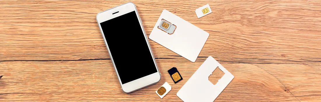 Un téléphone blanc à écran noir est posé à côté de cartes SIM blanches sur une table en bois.