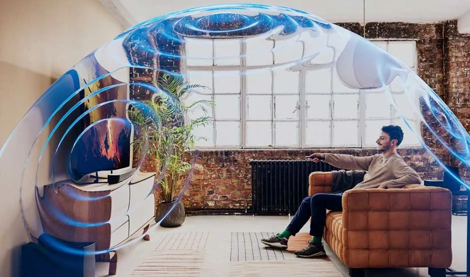 Un homme est assis sur un canapé et regarde la télévision; des ondes bleues illustrent un son immersif dans un loft lumineux.