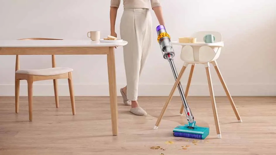 Une table en bois clair avec une chaise, un aspirateur bleu et argenté, et une chaise haute sur un sol en bois.