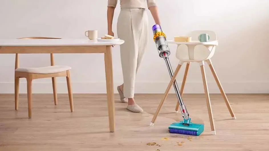 Une table en bois clair avec une chaise, un aspirateur bleu et argenté, et une chaise haute sur un sol en bois.