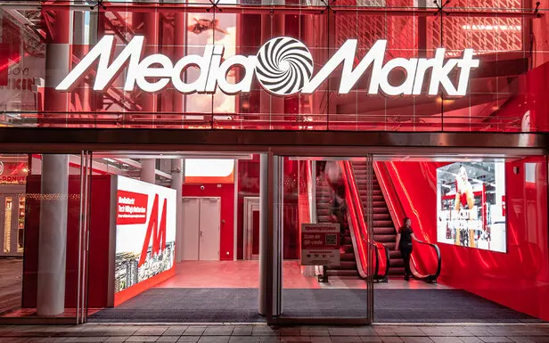Façade rouge et blanche du Media Markt avec escalators visibles à travers les fenêtres.