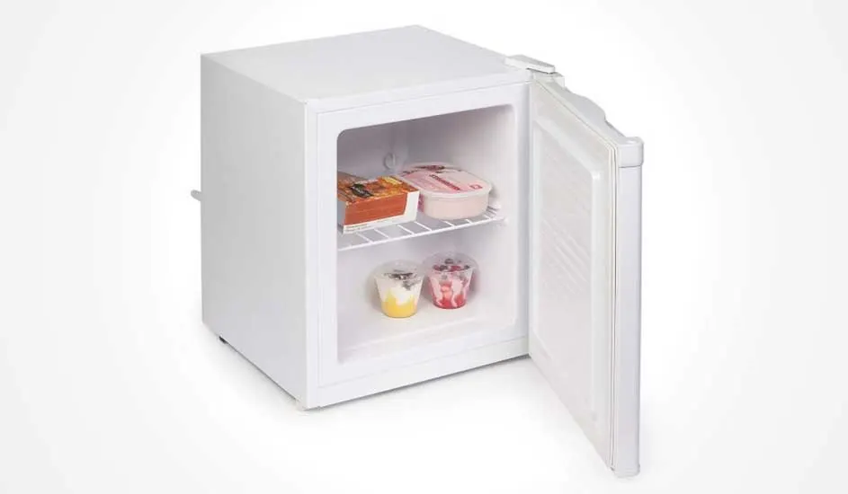 Een kleine witte vriezer met open deur, binnenin een draadrek met diepvriesmaaltijden, ijs en twee bekers dessert op de bodem.