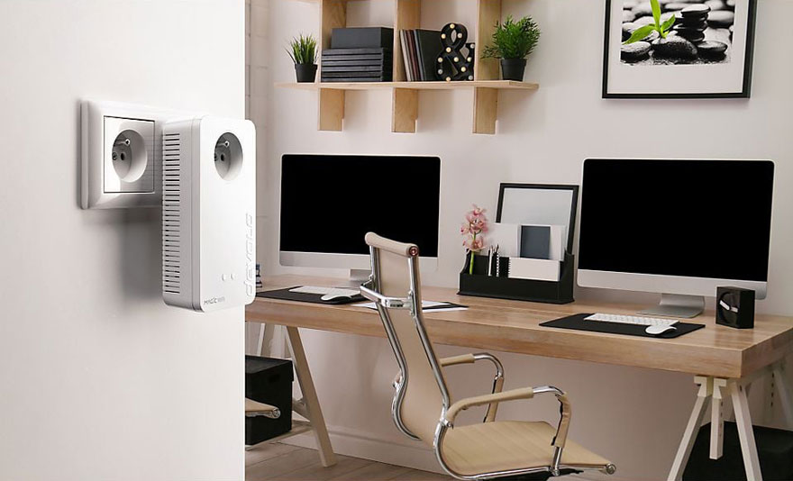 Een witte stekkerdoos is in een stopcontact gestoken, in een kamer met bureau en computers.