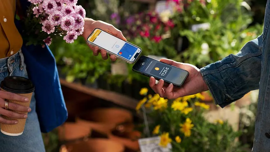 Deux smartphones effectuent un paiement sans contact près de fleurs colorées. Un gobelet à café est visible.