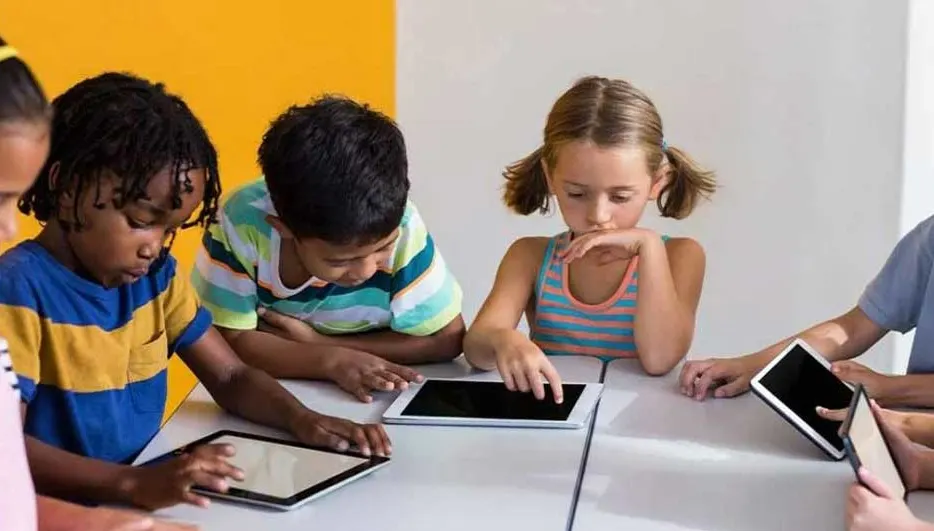Des enfants sont assis à une table blanche, utilisant des tablettes. Le fond est jaune et blanc.