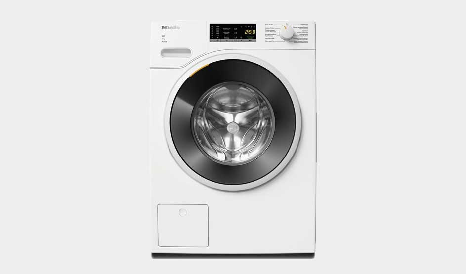 Een witte Miele wasmachine met een groot zwart deurvenster en digitaal display staat centraal in een moderne, lichte ruimte.