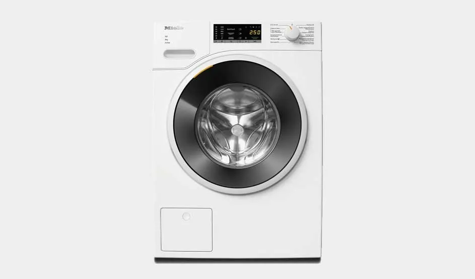 Front view of a white Miele washing machine with large dark door, shiny drum and a digital display with control dial on top against a light grey background.