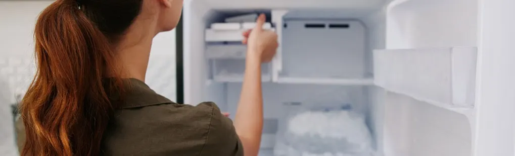 Une main actionne un distributeur de glaçons dans un réfrigérateur blanc. Des glaçons sont visibles en dessous.