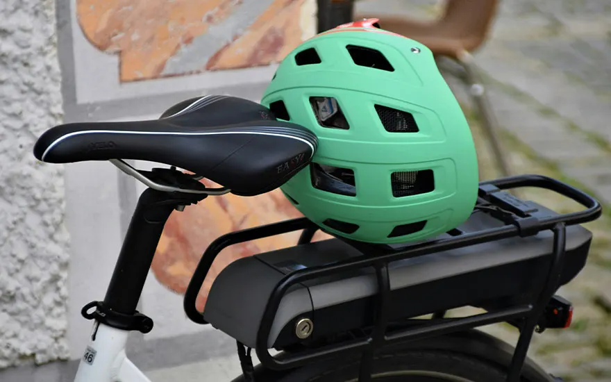 Un vélo a une selle noire et un casque vert dessus. Le porte-bagages noir est au-dessus de la roue arrière.