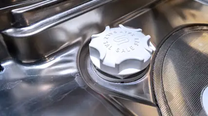 Een close-up van een witte zoutdop in een zilverkleurige vaatwasser, met de tekst "SALT / ZOUT" erop.