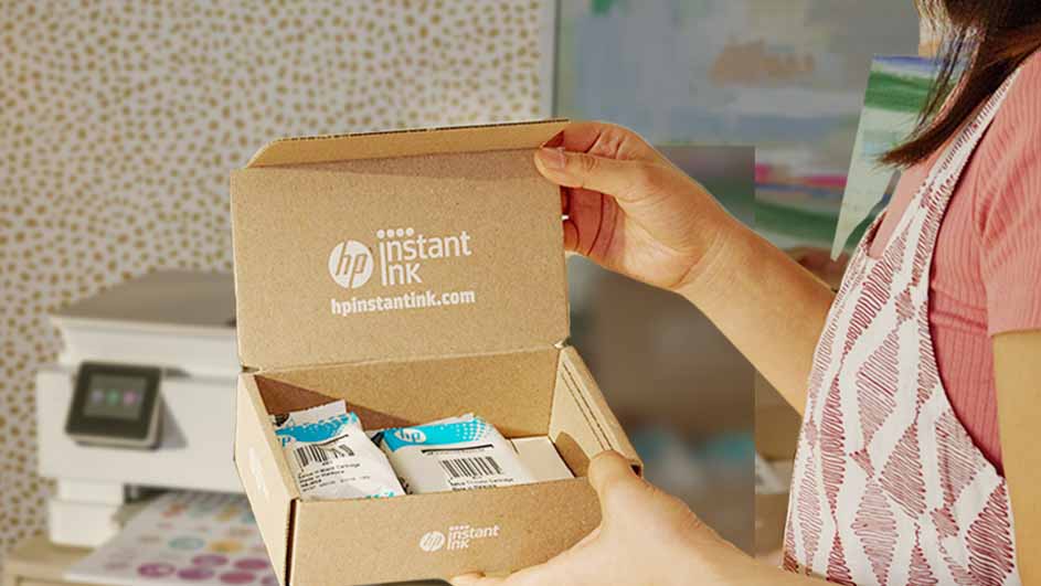 Een geopende bruine doos met HP Instant Ink-cartridges. Een witte printer staat op de achtergrond.
