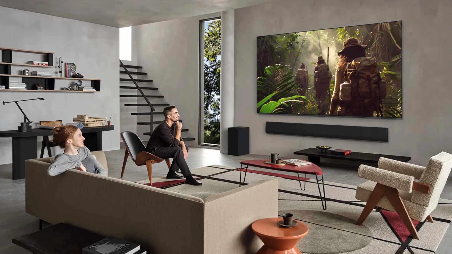 Salon moderne où deux personnes regardent un grand téléviseur affichant une scène d’aventure dans une jungle, avec une barre de son placée en dessous.